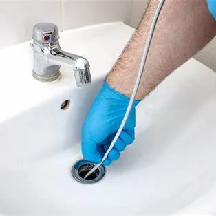 Gloved hand clearing a bathroom sink drain with a drain snake