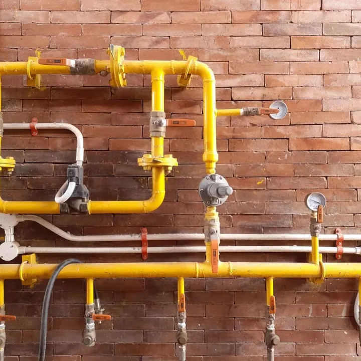 Yellow gas piping with a pressure gauge on a brick wall
