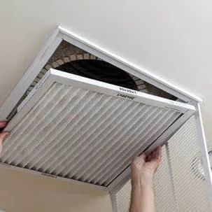 Hands fitting a pleated filter into a ceiling return grille